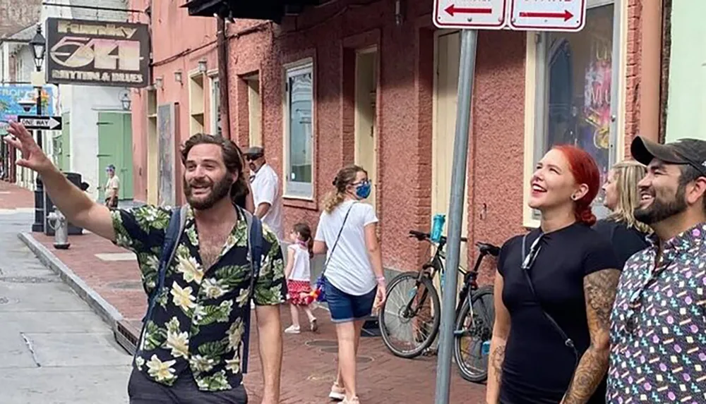 Three joyful people look upwards likely engaging with something off-camera on a city street with one man pointing while other individuals walk in the background near parked bicycles and street signs