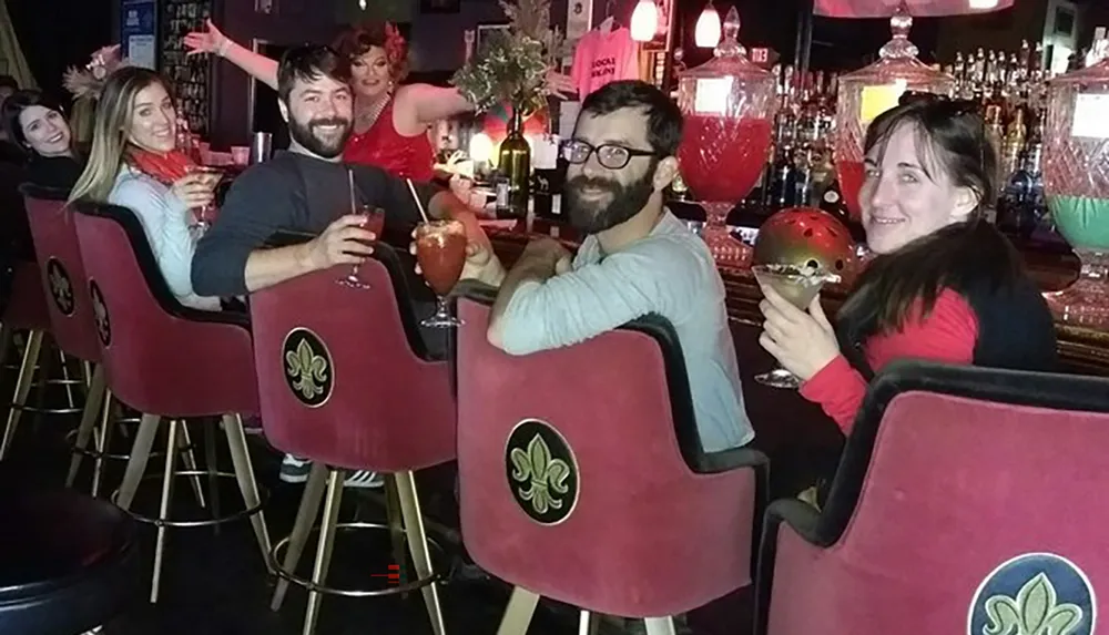 Several people are sitting at a bar smiling and holding cocktails having a good time together