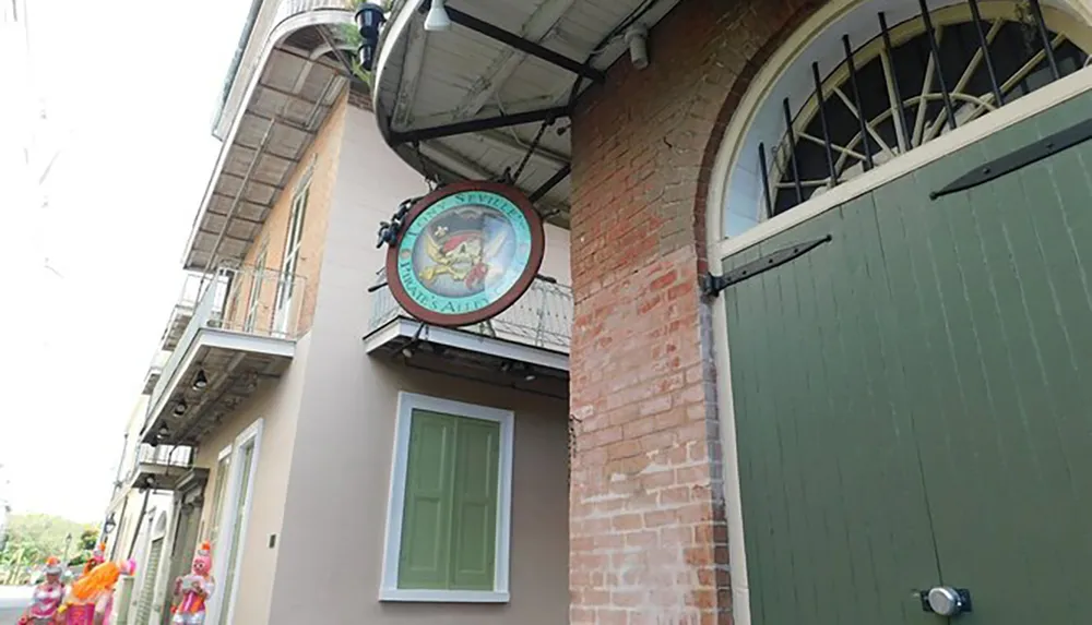 The image shows a traditional round pub sign with a picture of a rabbit playing a banjo affixed to the corner of a brick building with a balcony and green shutters