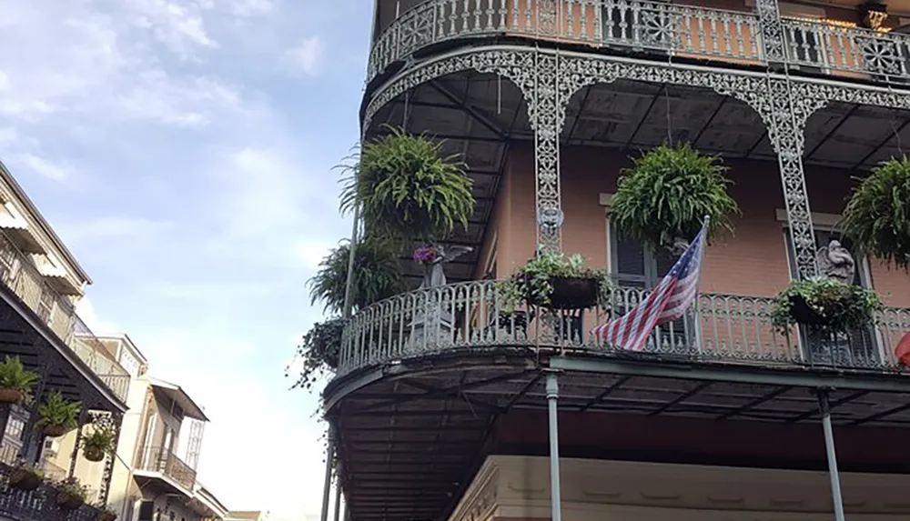 The image showcases a two-tiered wrought iron balcony adorned with green plants and an American flag characteristic of New Orleans French Quarter architecture