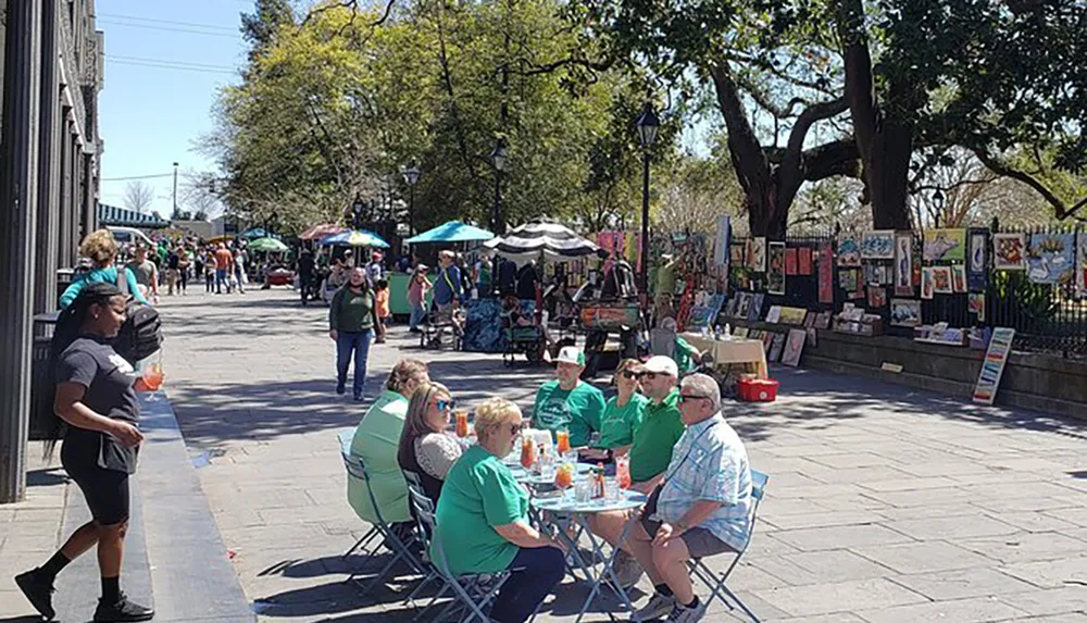 A lively outdoor market scene with people wearing green suggesting a festive occasion amidst art stalls and casual street dining under sunny skies