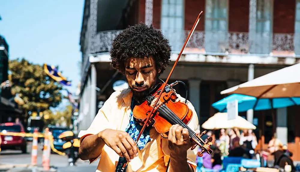 A street musician is intently playing the violin on a sunny day in an urban setting with outdoor dining in the background
