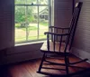 A wooden rocking chair is situated near a window with open shutters overlooking a street view outside a residential home