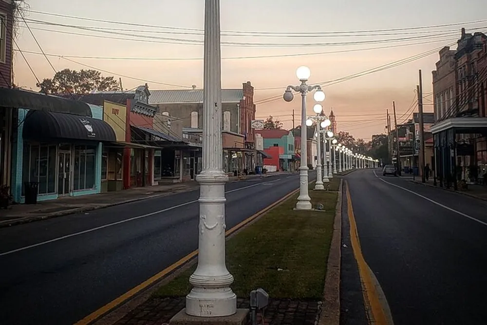 This image captures a serene dusky view of a quiet main street lined with vintage-style street lamps and old buildings exuding a small-town atmosphere