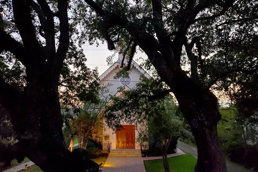 Twilight falls over a picturesque chapel framed by the dark silhouette of leafy trees