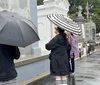 Four people are standing under umbrellas in the rain looking at a wall with names inscribed on it possibly at a memorial or cemetery