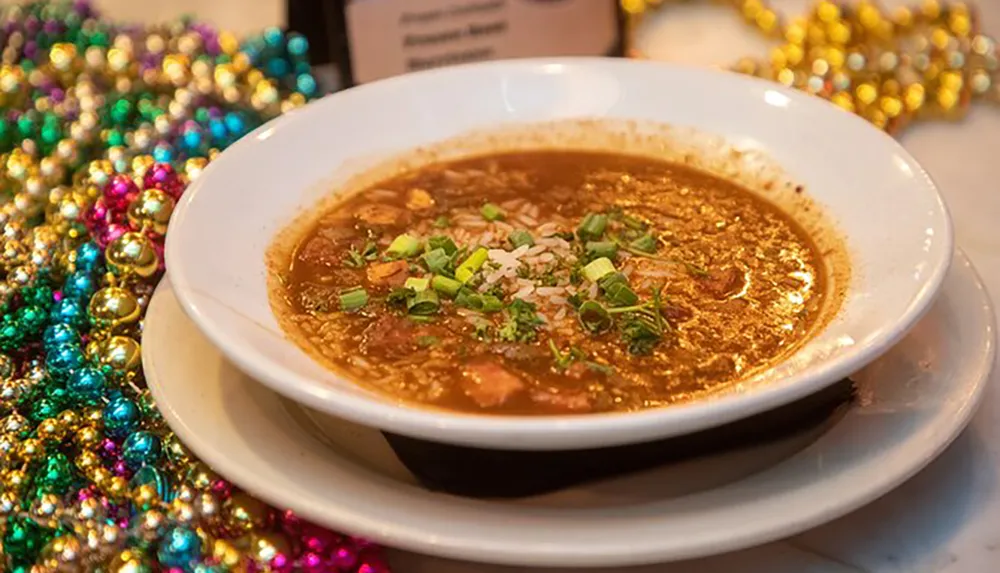 A bowl of gumbo is surrounded by Mardi Gras beads suggesting a festive celebration of Louisiana cuisine