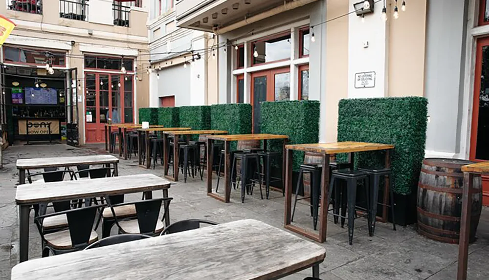 Outdoor seating at a pub or restaurant with various wooden tables barrel-based tables and faux green hedges providing a cozy urban alfresco dining setting