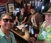 A group of five people is smiling for a selfie inside a bar with some holding drinks and phones on the bar top