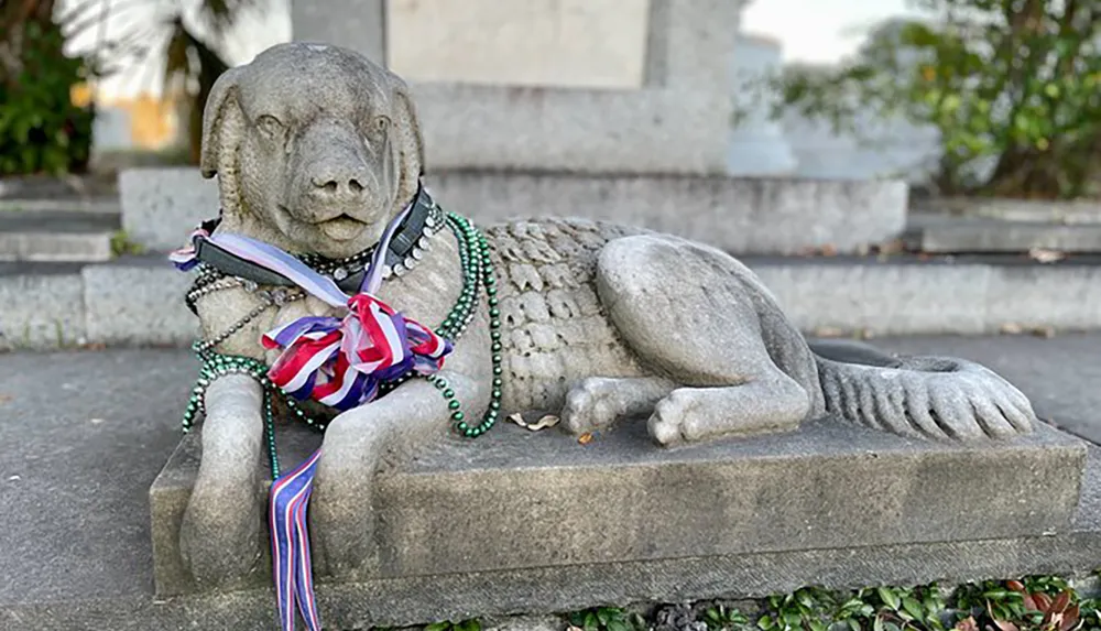 The image shows a stone statue of a dog adorned with colorful beads and ribbons