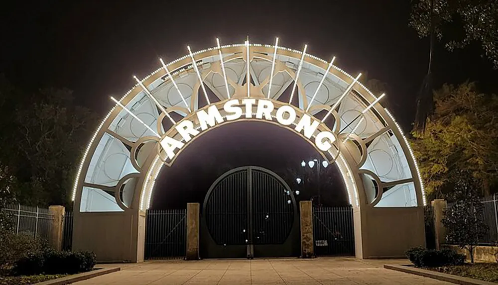 The image shows the illuminated entrance arch reading ARMSTRONG at night likely representing the gateway to a park or venue