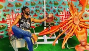 A man is joyfully posing next to an oversized model of a lobster, with a colorful seafood-themed backdrop and props creating a playful scene.