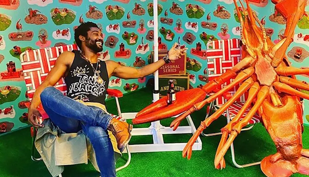 A man is joyfully posing next to an oversized model of a lobster with a colorful seafood-themed backdrop and props creating a playful scene