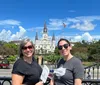 Two people are smiling in front of the historic St Louis Cathedral in Jackson Square New Orleans on a sunny day with horse-drawn carriages visible in the background