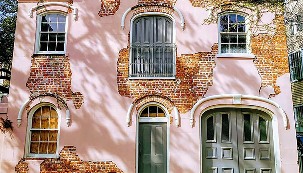 The image shows a pink facade with exposed brick patches around arched windows and doors giving the building a charming weathered look