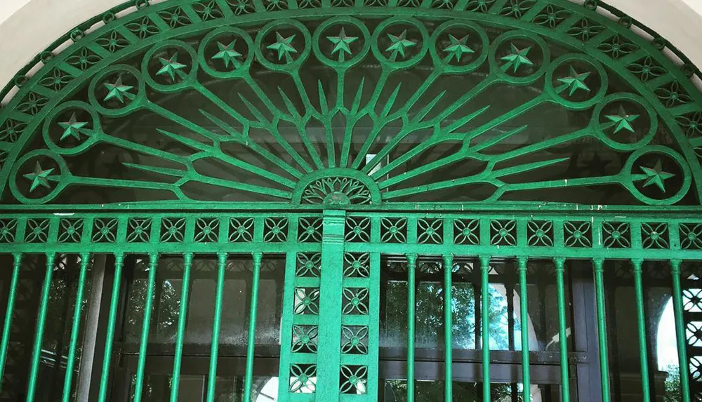 The image shows a green ornate metal gate featuring a semicircular transom with star-like patterns at the top and vertical bars with decorative motifs below