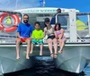 A family wearing snorkeling gear is posing for a photo in shallow waters with a boat in the background