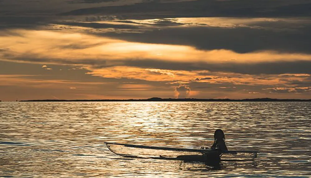 The image shows a lone kayaker on a calm sea with the horizon aglow during a golden sunset