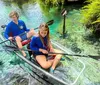 Two people are kayaking in clear water above an underwater scene of rocks and plants with the kayaks clear bottom offering a view into the pristine aquatic environment