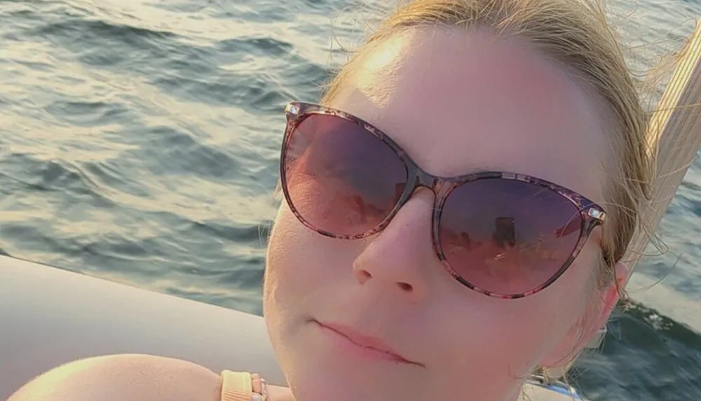 The image shows a person wearing sunglasses with a body of water in the background likely signaling that they are on a boat enjoying a sunny day