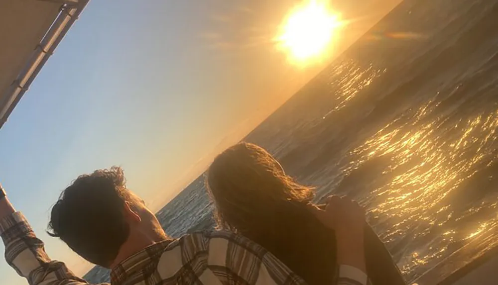 Two people are enjoying a sunset together on a boat silhouetted against the shimmering water