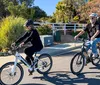 Two individuals are enjoying a sunny day while riding bicycles on a path with lush vegetation around them