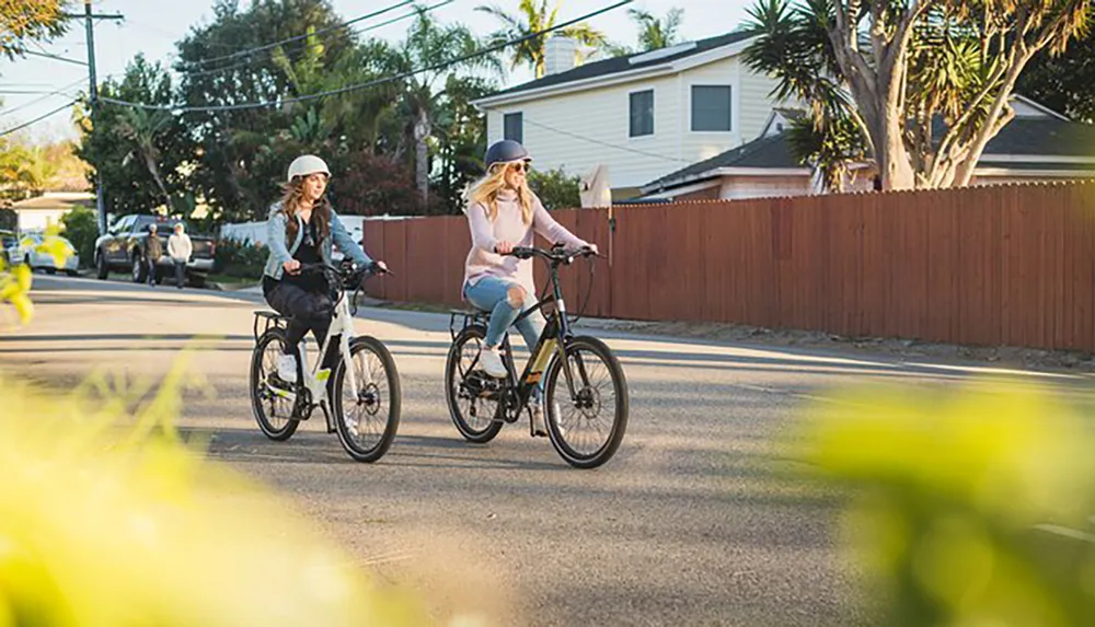 Two individuals are riding bicycles leisurely down a residential street with the late afternoon sun casting warm light on the scene