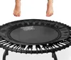 A person stands barefoot on a mini trampoline with other trampolines visible in the background suggesting this is a fitness or exercise setting