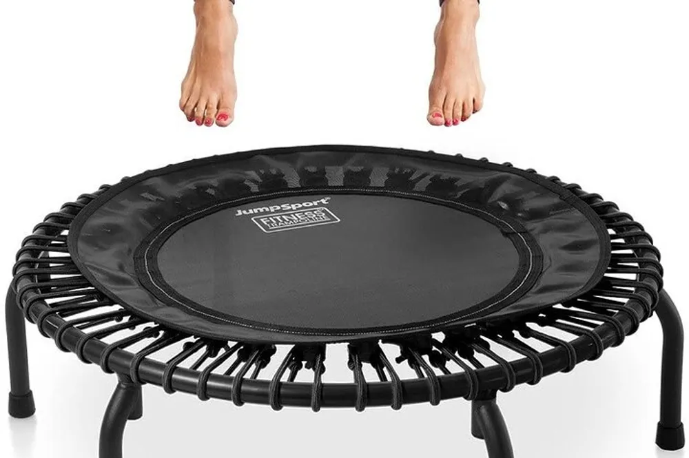 A person is about to use a black mini fitness trampoline with only their lower legs and feet visible in the frame
