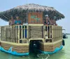 A group of people is enjoying a sunny day on a unique tiki bar-themed boat floating on calm water
