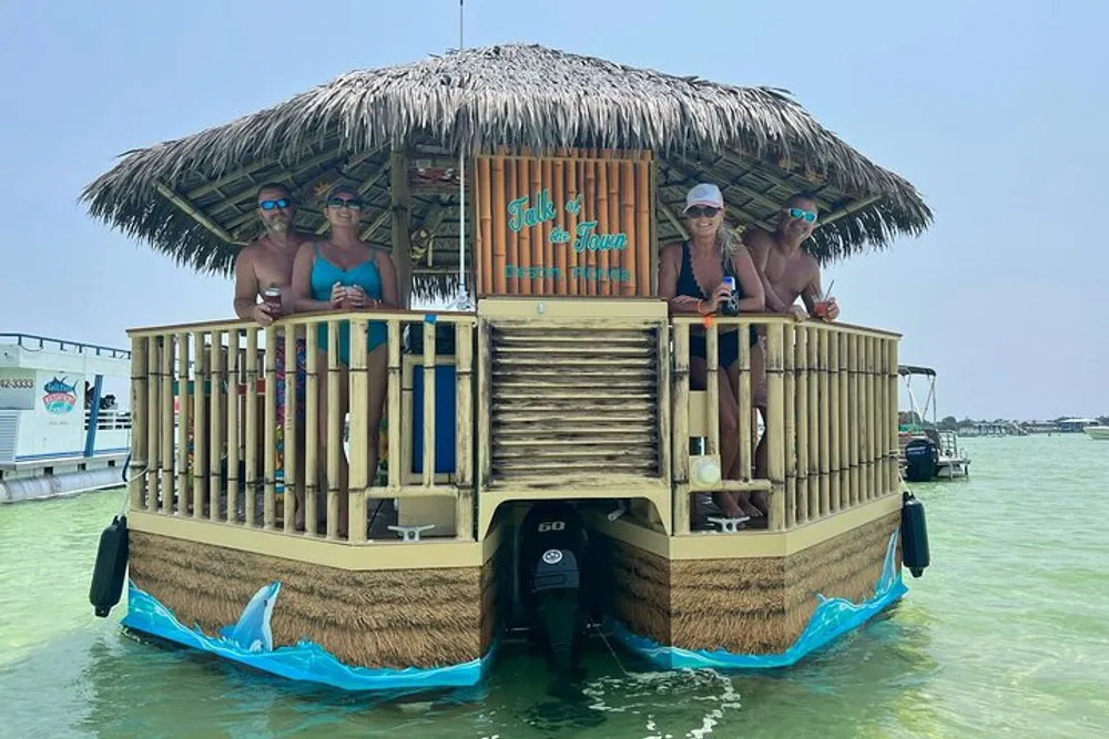 A group of people is enjoying a sunny day on a unique tiki bar-themed boat floating on calm water