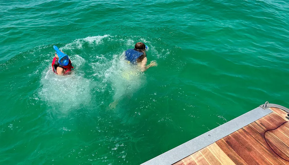 Two individuals are seen snorkeling in clear green waters near a boat