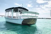 A white passenger boat with a dark canopy is floating on clear turquoise waters, showcasing the boat's name and website on its hull.