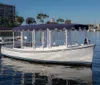 A white boat with a purple canopy is floating on calm waters near a waterfront with buildings in the background