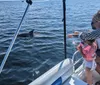 An adult and a child are pointing towards a dolphin near a boat on a sunny day