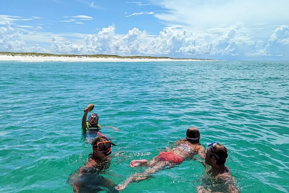 Three people with snorkeling gear are enjoying clear turquoise waters with a beach visible in the background