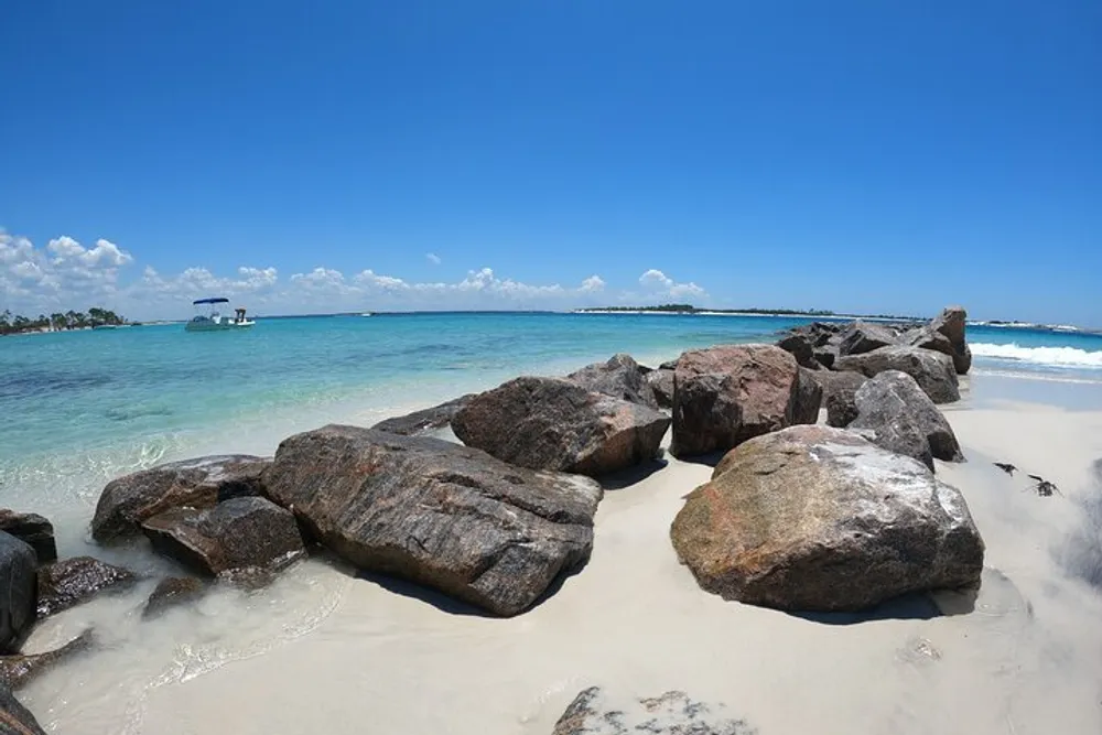 A serene beach scene with large rocks in the foreground and a view of clear turquoise waters under a blue sky