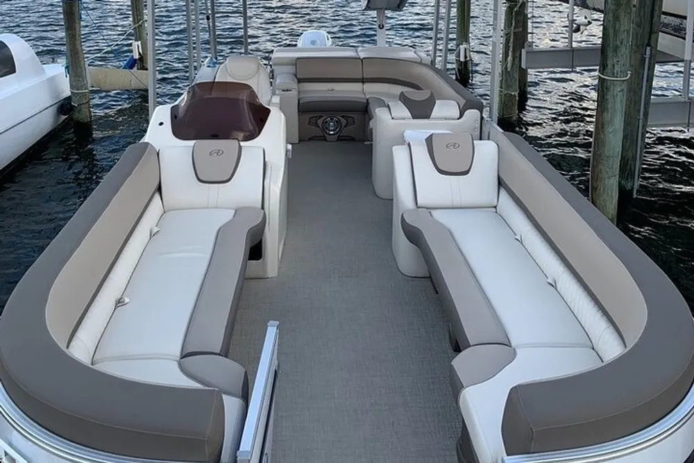 The image shows the interior of a modern pontoon boat with spacious and comfortable seating docked in a marina