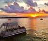A pontoon boat with passengers cruises on a calm waterway against the backdrop of a vivid sunset and scattered clouds