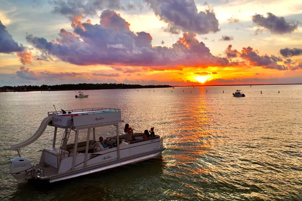 A pontoon boat with passengers cruises on a calm waterway against the backdrop of a vivid sunset and scattered clouds