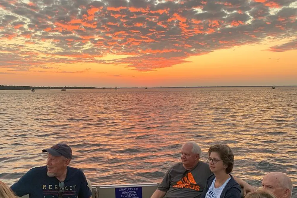 The image shows a group of people enjoying a picturesque sunset over a body of water creating an ambiance of warm vibrant colors across the sky and waters surface