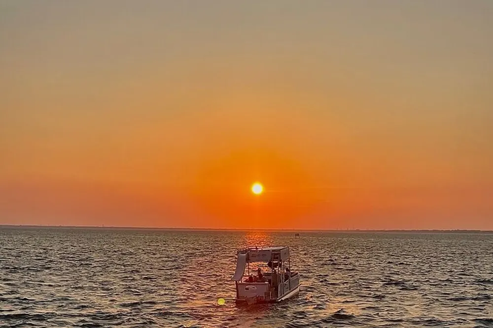 A boat is floating on the water against a backdrop of a beautiful orange sunset over the ocean