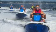 A group of people is enjoying a lively jet ski ride on a sunlit body of water.