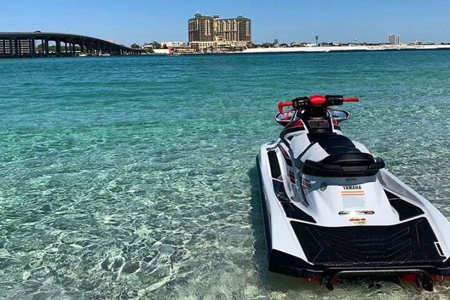 A jet ski is floating on clear turquoise waters near a coastline with a bridge and buildings in the background.
