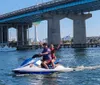 A jet ski is floating on clear turquoise waters near a coastline with a bridge and buildings in the background