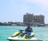 A jet ski is floating on clear turquoise waters near a coastline with a bridge and buildings in the background