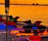 The image shows a group of illuminated transparent kayaks at nighttime glowing with a vibrant array of colors by the waters edge