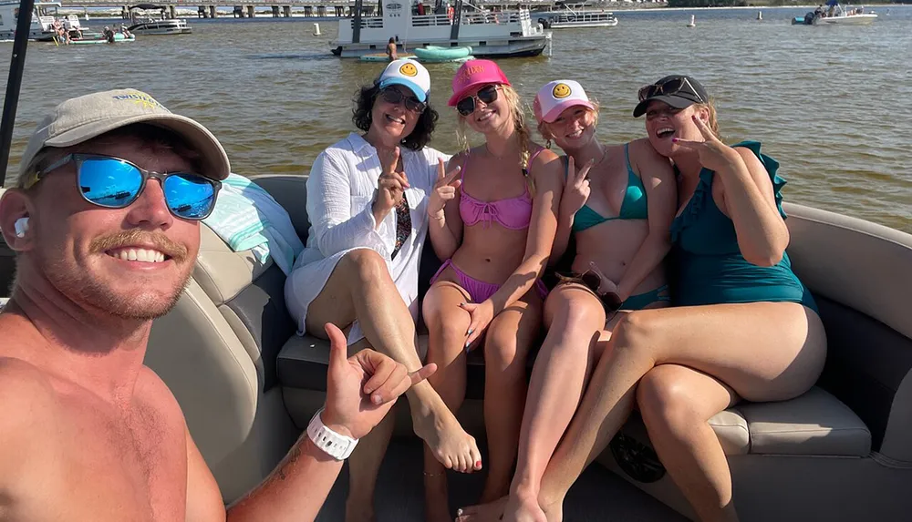 A group of five people is smiling and posing playfully for a selfie aboard a boat on a sunny day