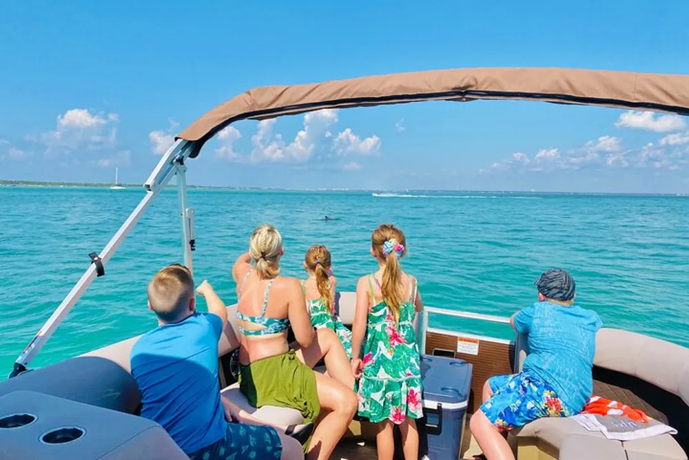 A group of people is sitting at the back of a boat enjoying the view of a clear turquoise sea under a sunny sky