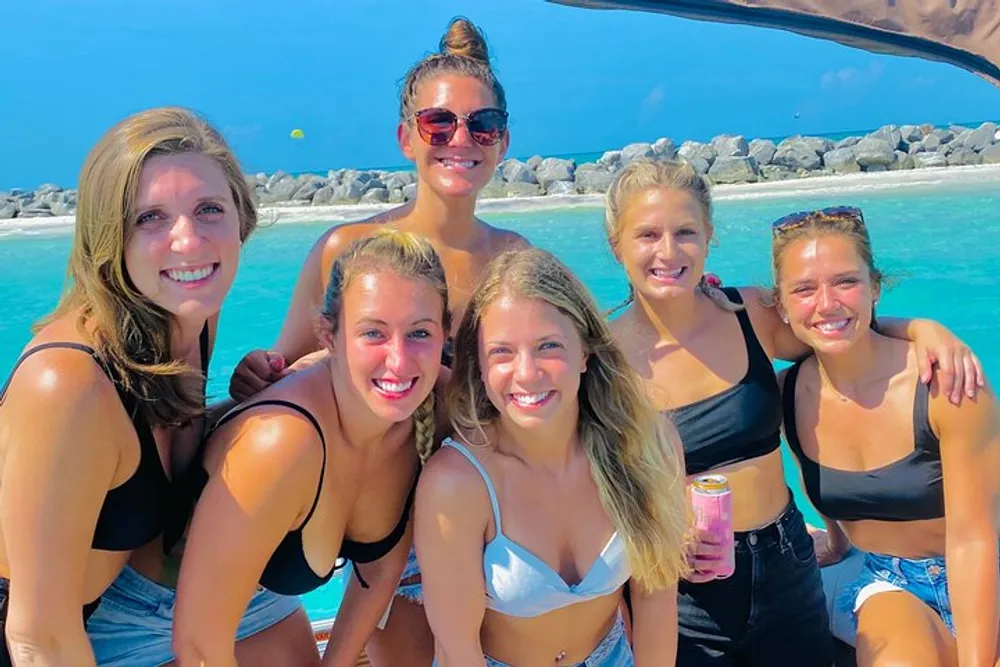 A group of smiling people posing for a photo on a sunny beach with clear blue skies and crystal-clear waters in the background